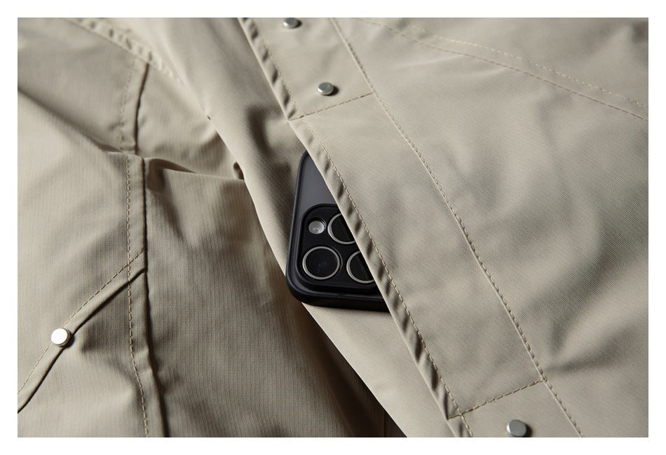 Close-up showing a phone tucked into a pocket on a taupe jacket, with stitched seams and metal snaps.