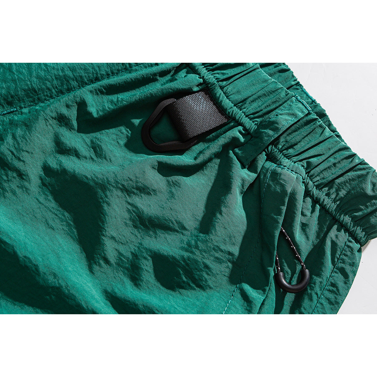 Close-up of teal shorts showing the elastic waistband, a black webbing loop and a side clip.