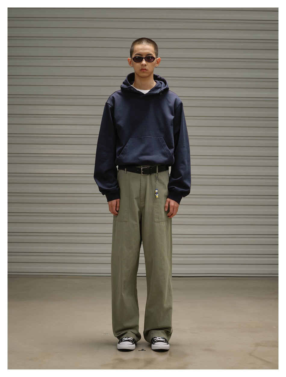 Model wearing olive green wide-leg utility pants with a black belt, navy hoodie and black sneakers, front view