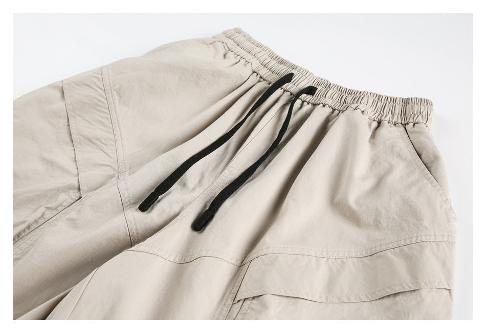Close-up of beige pants with an elastic waistband, black drawstrings, and stitched panel seams.