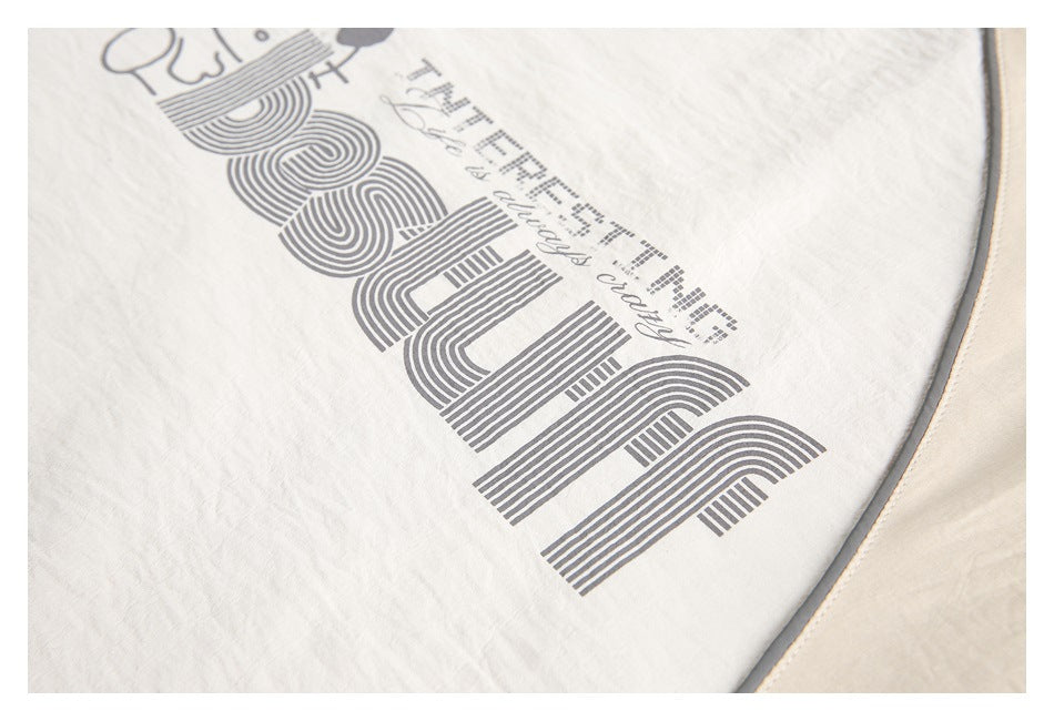 Tight crop of the gray striped lettering printed on a cream top, beside gray piping.