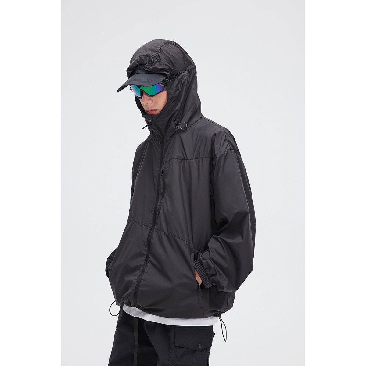 Model wearing a black hooded jacket with a cap and mirrored sunglasses, shown from the front at an angle.