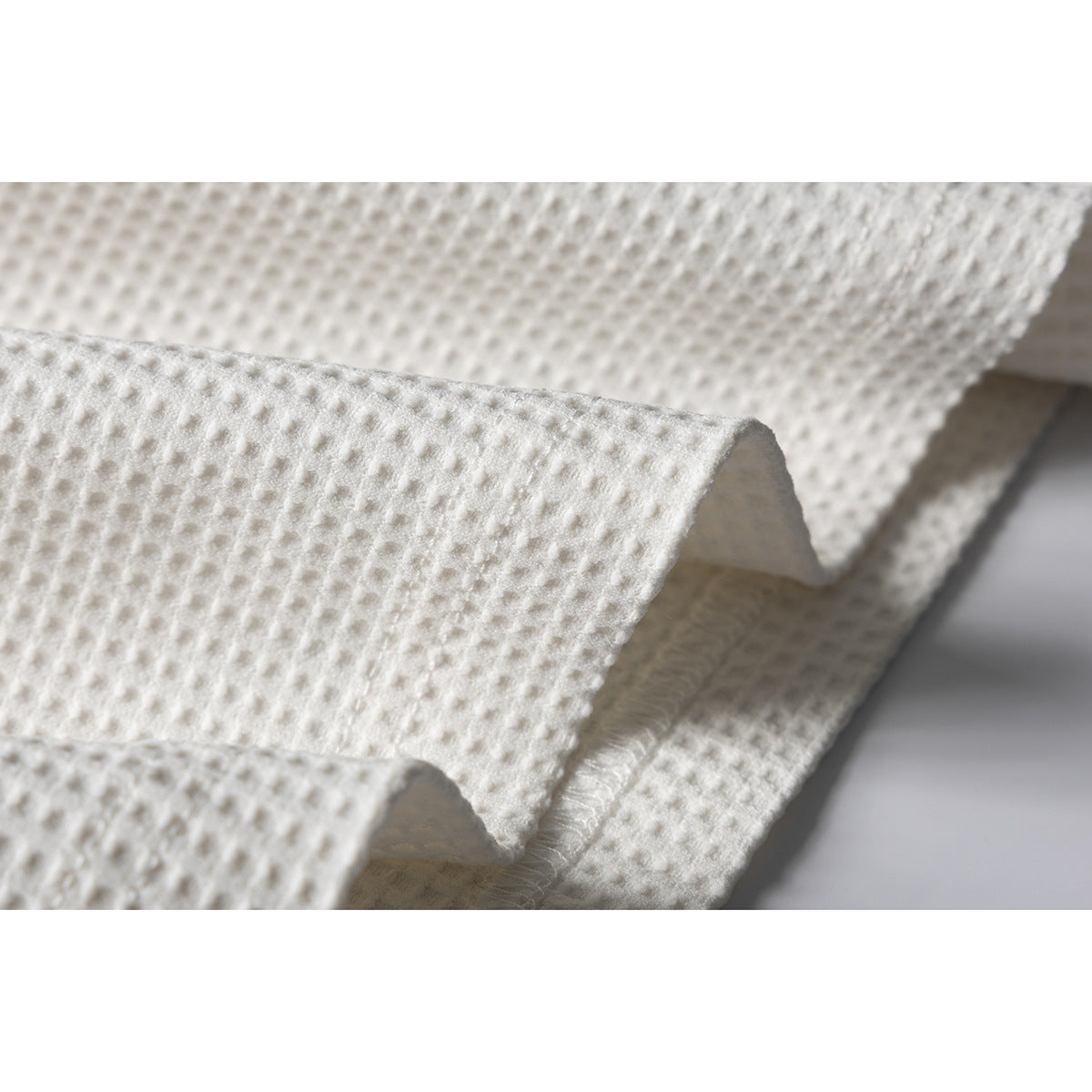 Close-up of ivory waffle-textured fabric folded to show its surface and stitched edge.