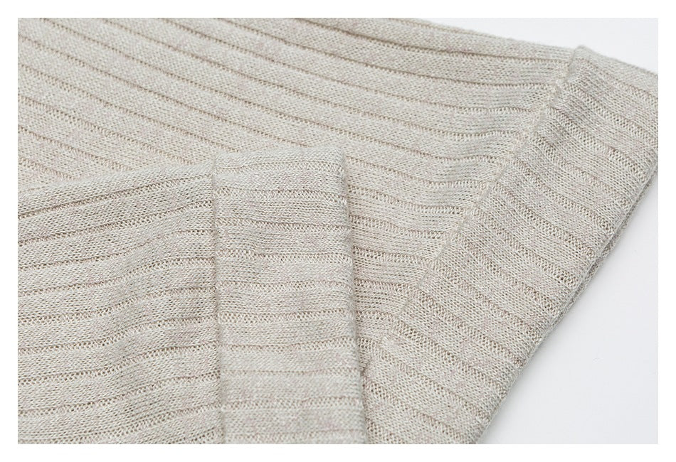Close-up of beige knit fabric with subtle vertical stripes, folded layers, and a ribbed edge.