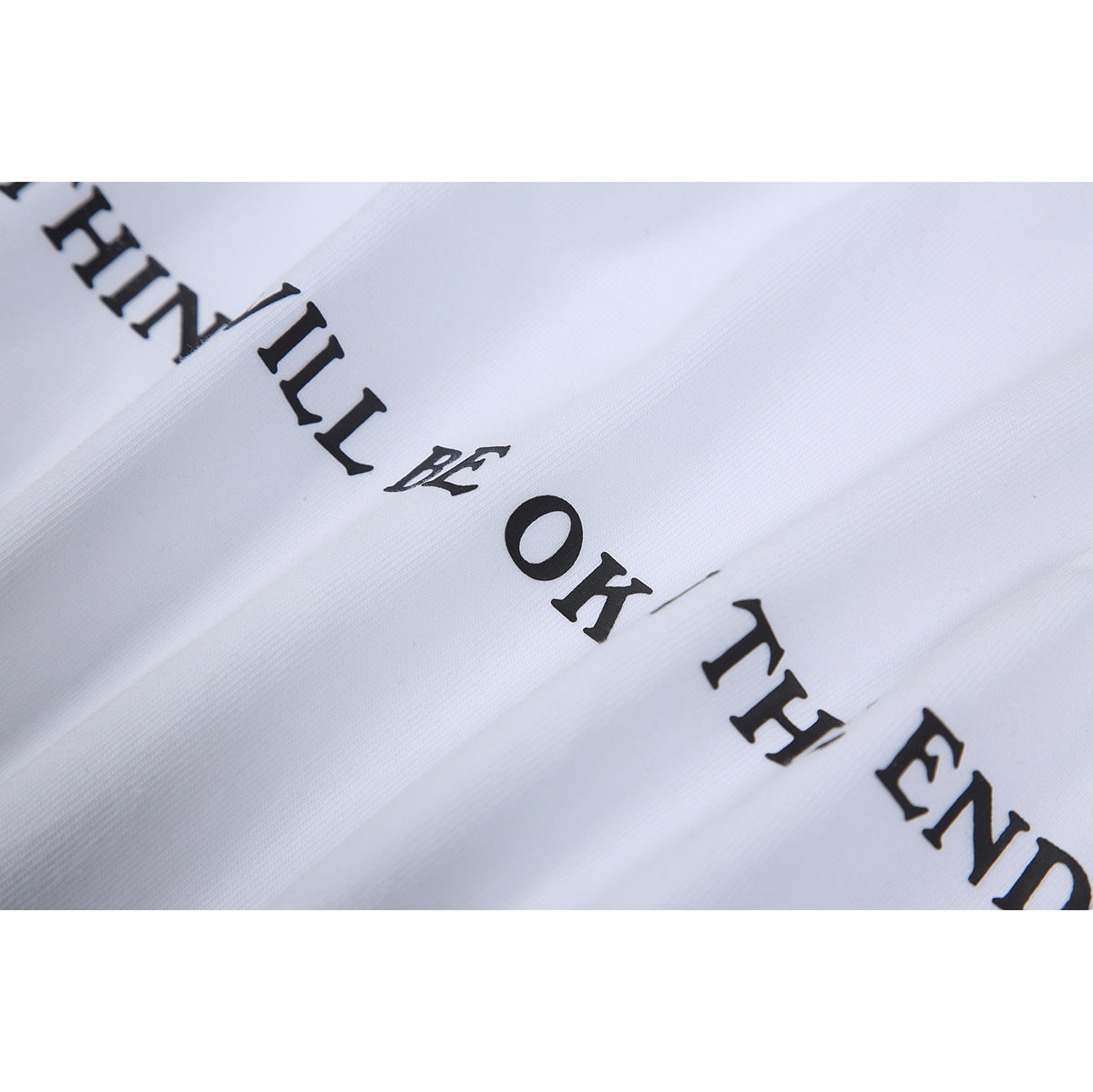 Close-up of black English lettering printed on white fabric, reading part of “Everything will be OK in the end.”