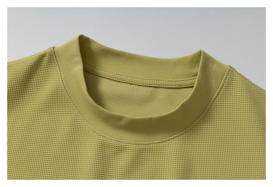 Close-up of the olive-yellow shirt’s ribbed crew neckline and perforated knit texture.