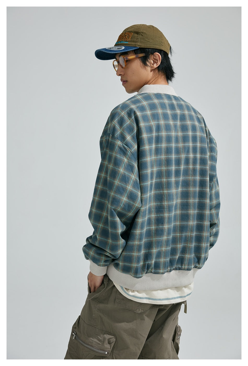 Model shown from behind wearing a blue plaid jacket with white ribbed trim and an olive cap.