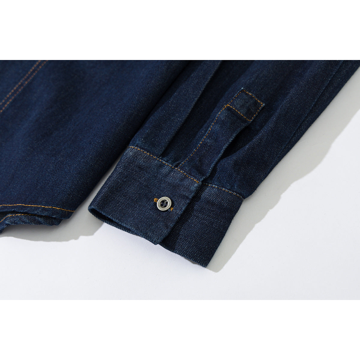 Close-up of a dark indigo denim shirt sleeve cuff with a button and contrast stitching.