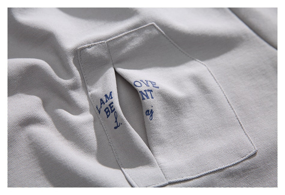 Close-up of a light gray shirt pocket with blue lettering visible across its folded opening.