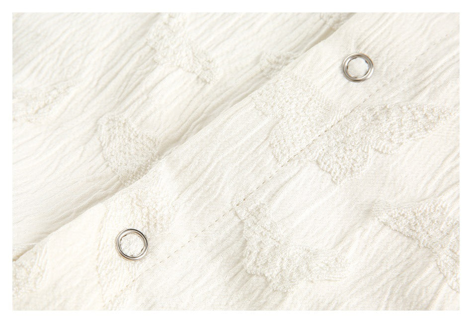 Ivory textured fabric with raised motifs and two small metal eyelets along a seam.