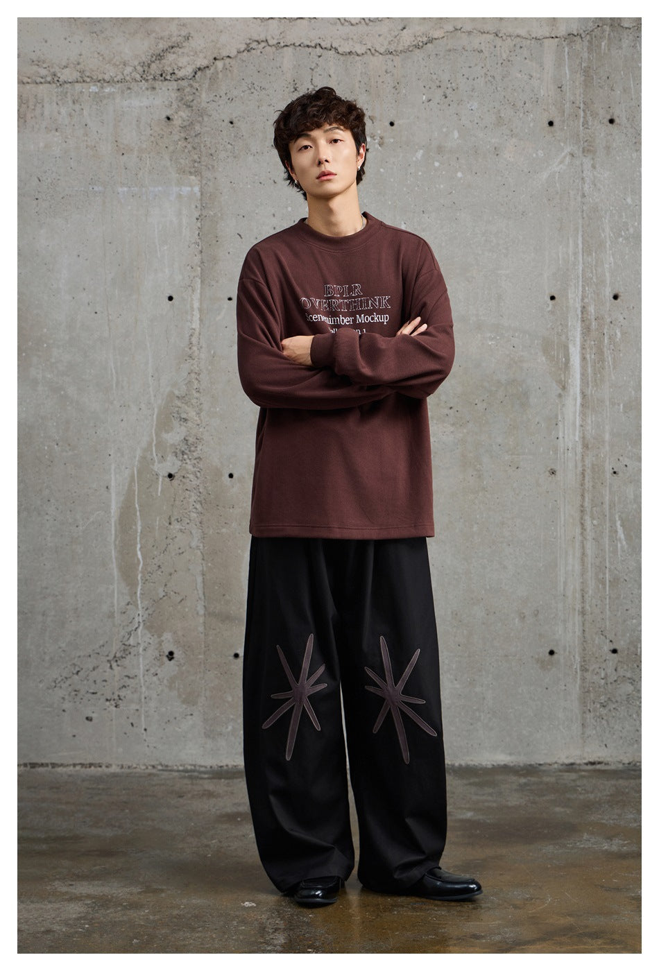 Full-length front view of a model in a burgundy oversized printed sweatshirt and black wide-leg trousers with starburst