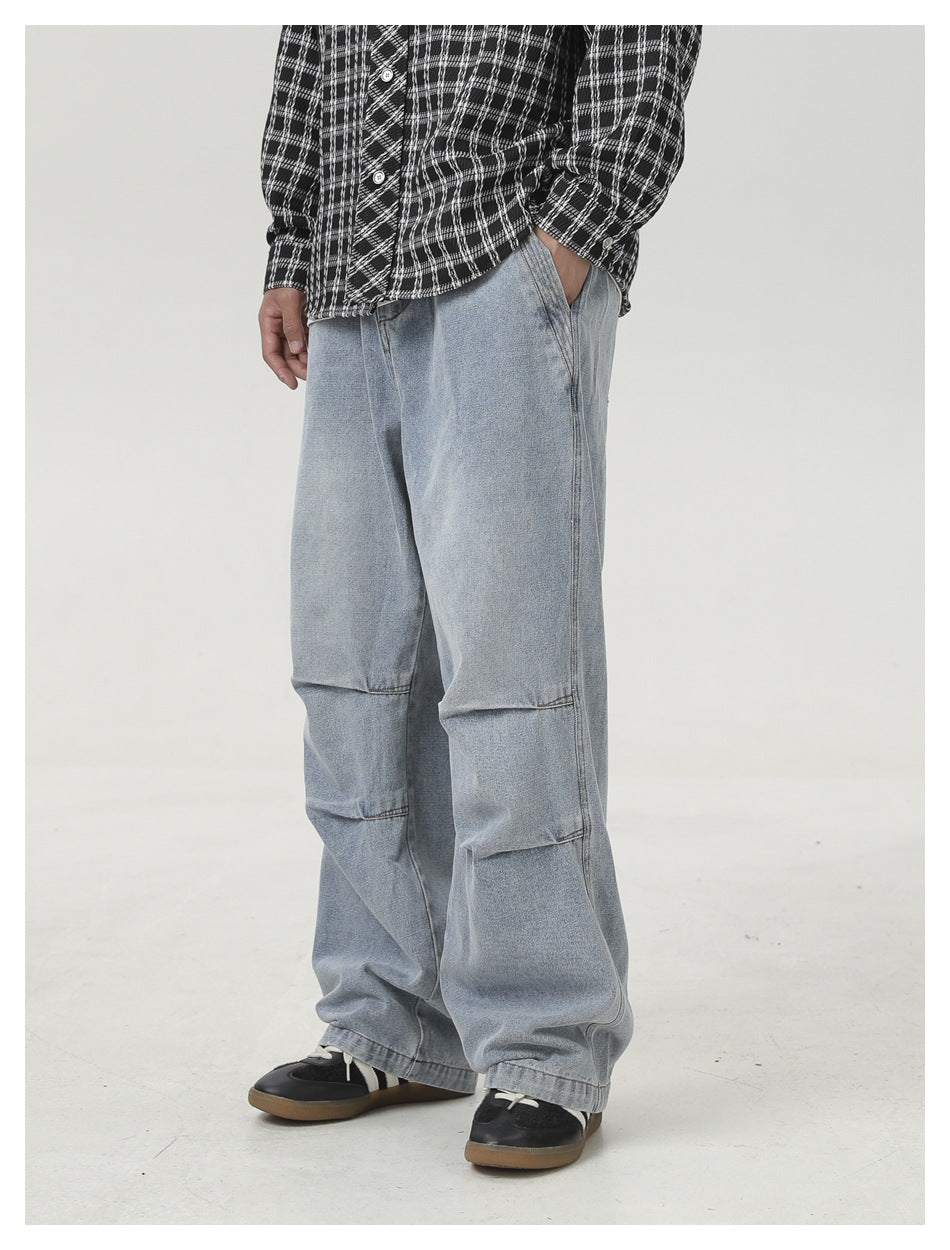 Angled view of loose light-wash jeans with layered knee seams, worn with a black-and-white plaid shirt.