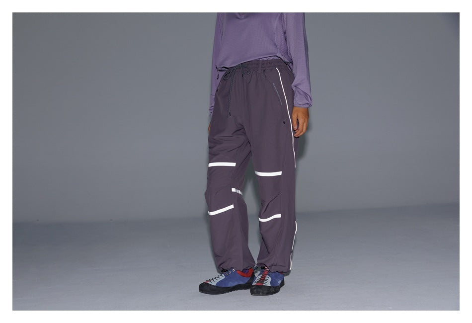 Three-quarter front view of dark plum drawstring pants with white reflective bands and side piping, worn by a model.