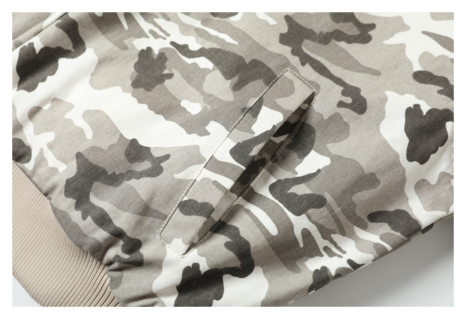 Close-up of a slanted welt pocket and beige ribbed hem on a gray and white camouflage jacket.