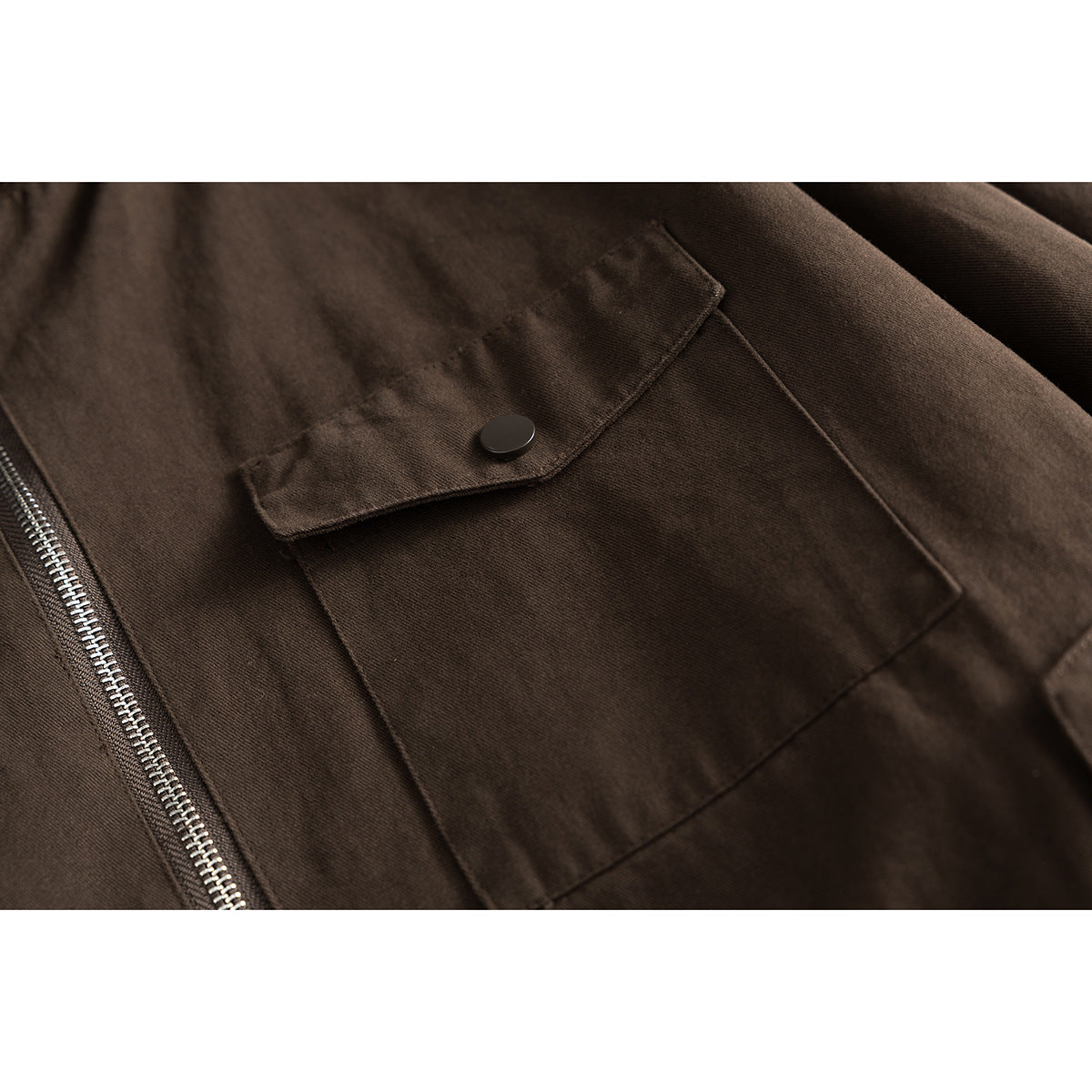 Close-up of a dark brown jacket’s large snap-flap pocket and silver front zipper.