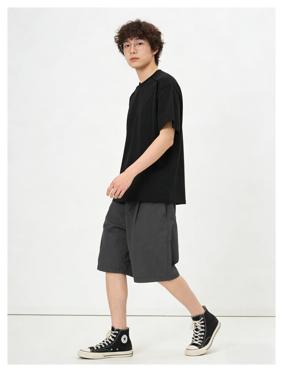 Model wearing a black relaxed T-shirt with gray shorts and black high-top sneakers, side view