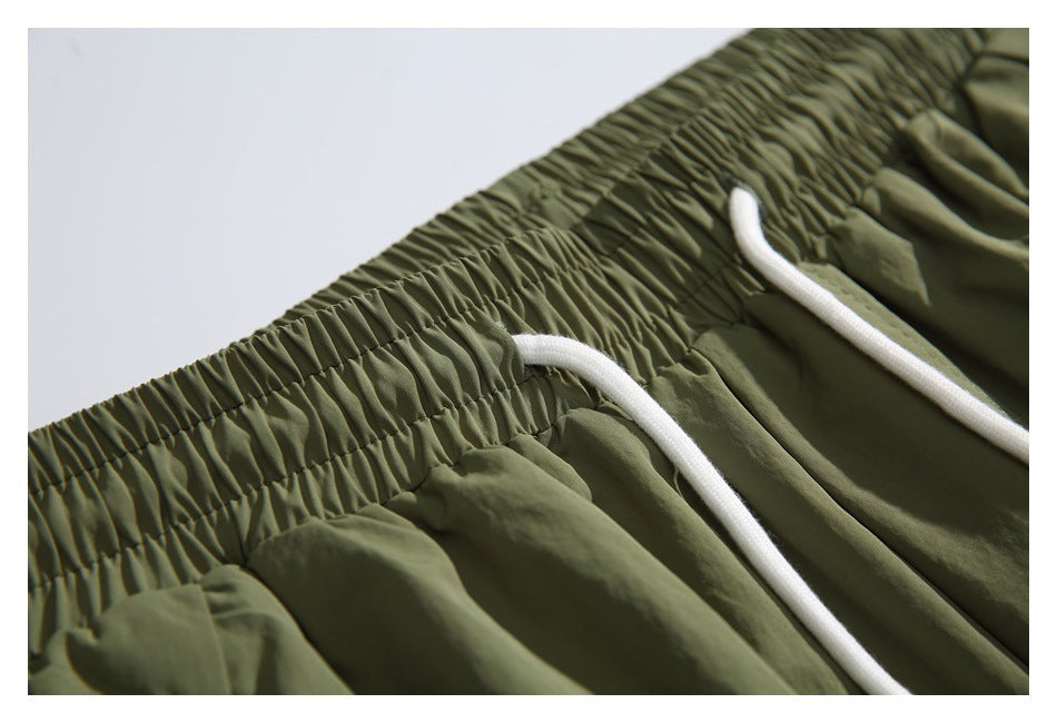 Close-up of olive-green pants with a gathered elastic waistband and white drawstrings.