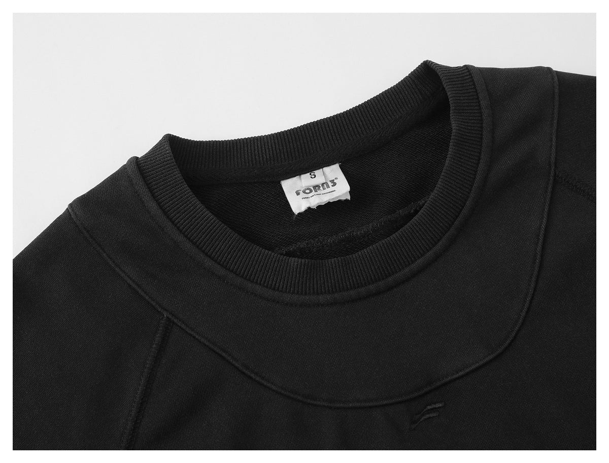 Close-up of a black crewneck sweatshirt showing its ribbed collar, curved chest seam, and small embroidered emblem.