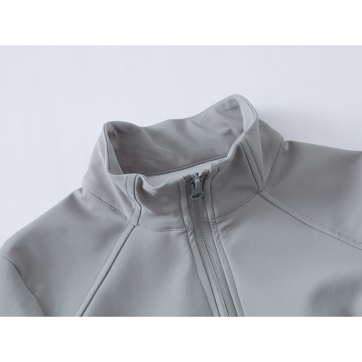 Close-up of a light gray jacket's high stand collar, center zipper, and stitched shoulder panels.