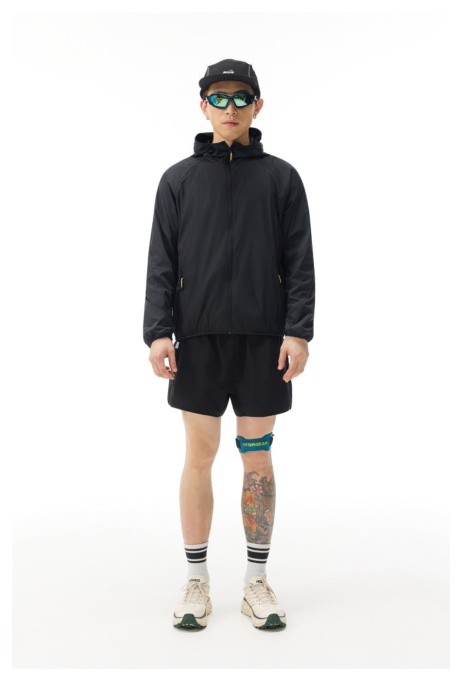 Man modeling a black hooded jacket and black shorts against a white background.