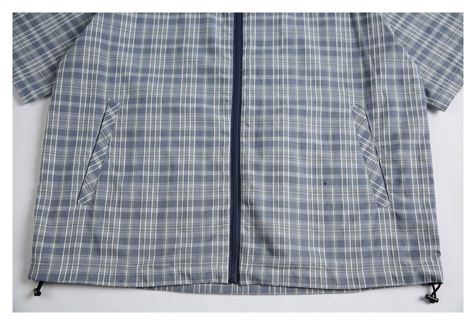 Cropped front view of a blue-gray plaid zip jacket with angled pockets and drawcords at the hem.