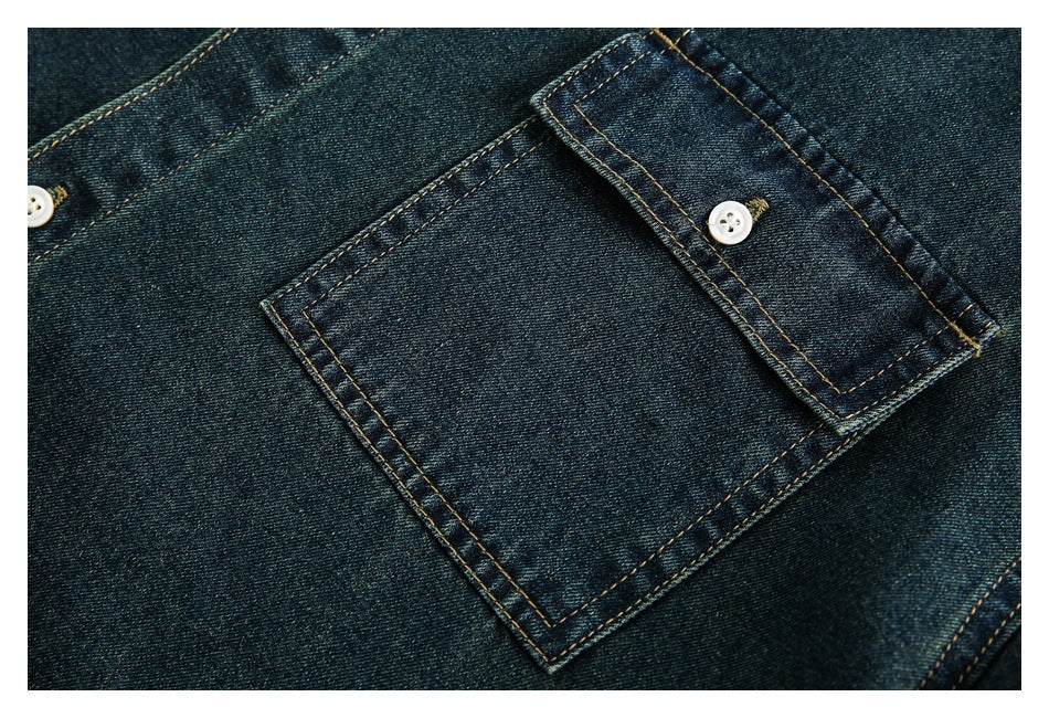 Close-up of a button-flap chest pocket on a dark indigo denim shirt with tan stitching.