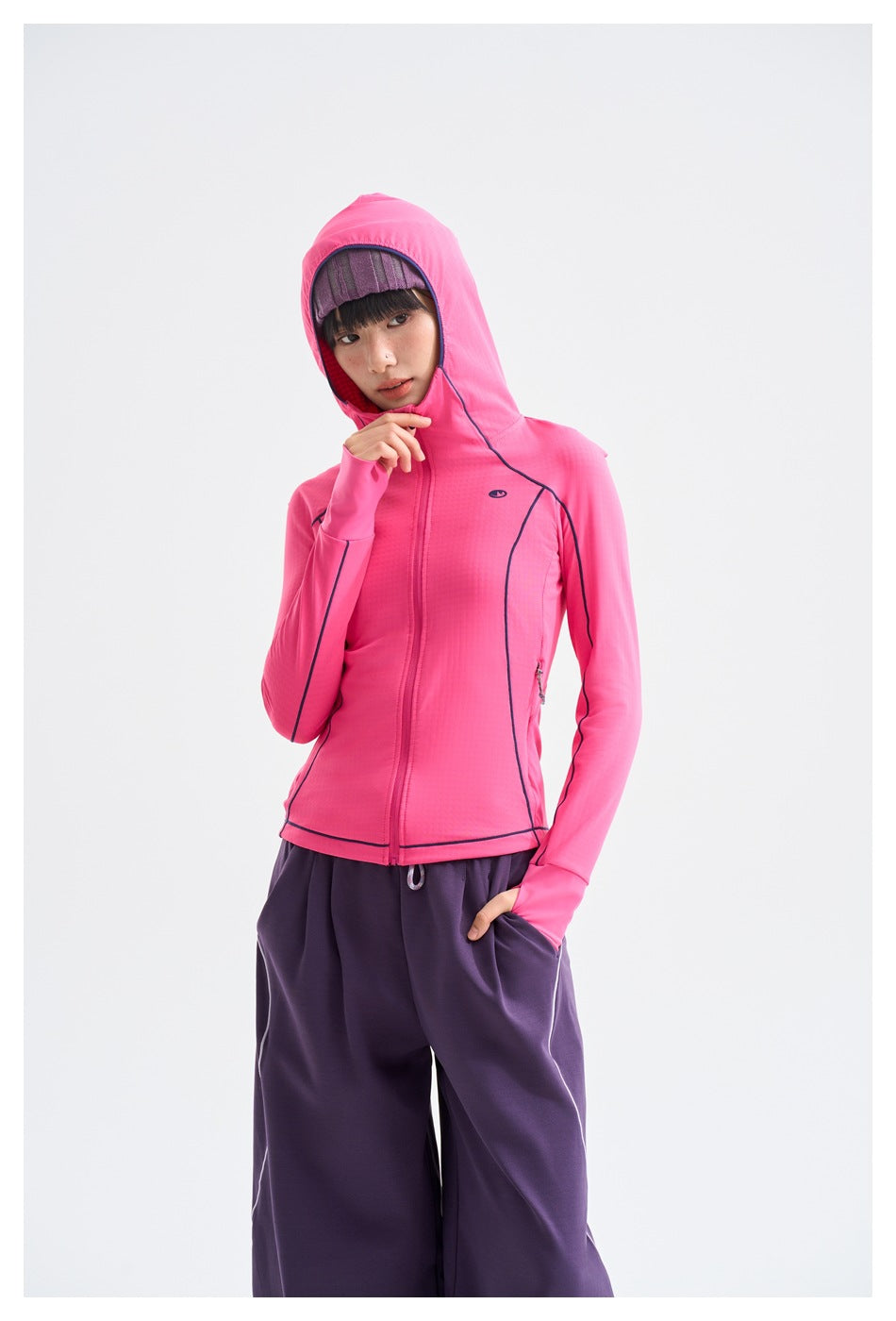 Model wearing a bright pink hooded zip jacket with navy piping and purple pants, shown from the front.