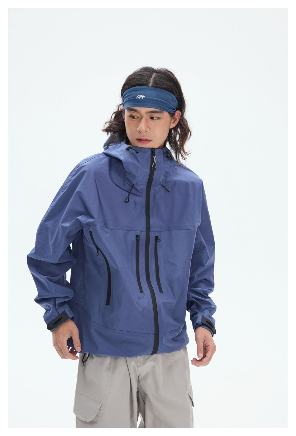 Close view of a model wearing a blue hooded jacket with a front zipper, multiple black zip pockets, and adjustable cuffs.