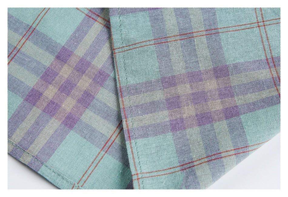 Close-up of plaid shirt fabric and intersecting stitched seams in mint, lavender, gray, and rust-red.