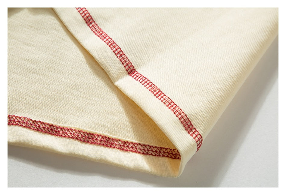 Close-up of folded cream fabric showing red overlock stitching along the seams.
