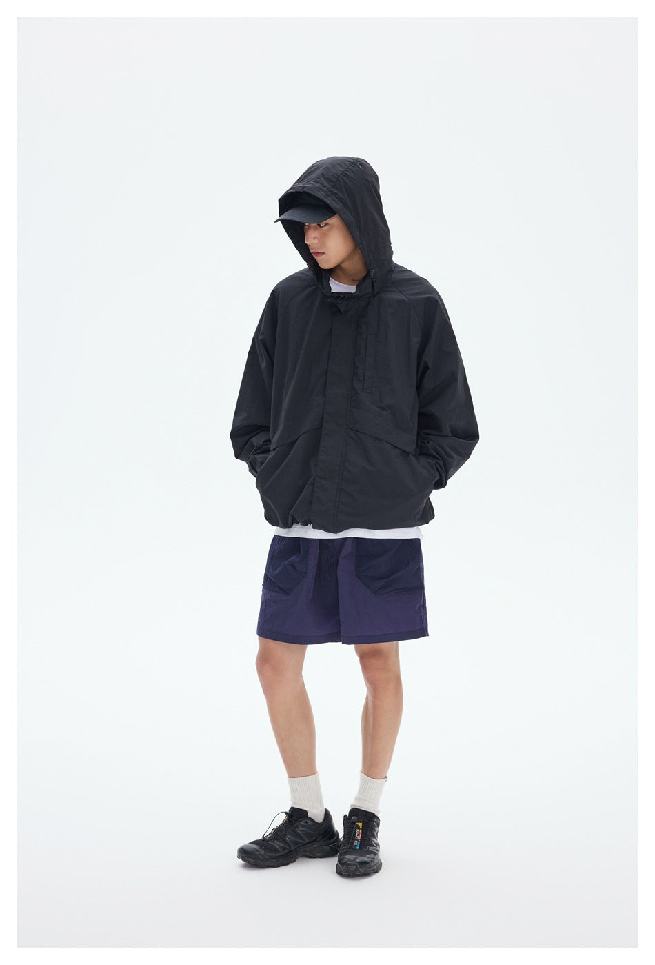 Model wearing a black hooded jacket with purple shorts, shown from the front against a light background.