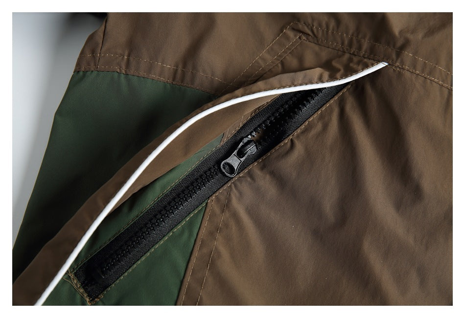 Close-up of a brown and dark green jacket showing a black zippered pocket and white piping.