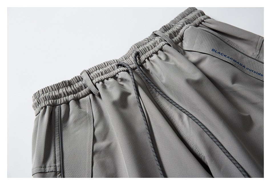 Close-up of gray pants showing the gathered drawstring waistband, pocket seam and small lettering on the garment.