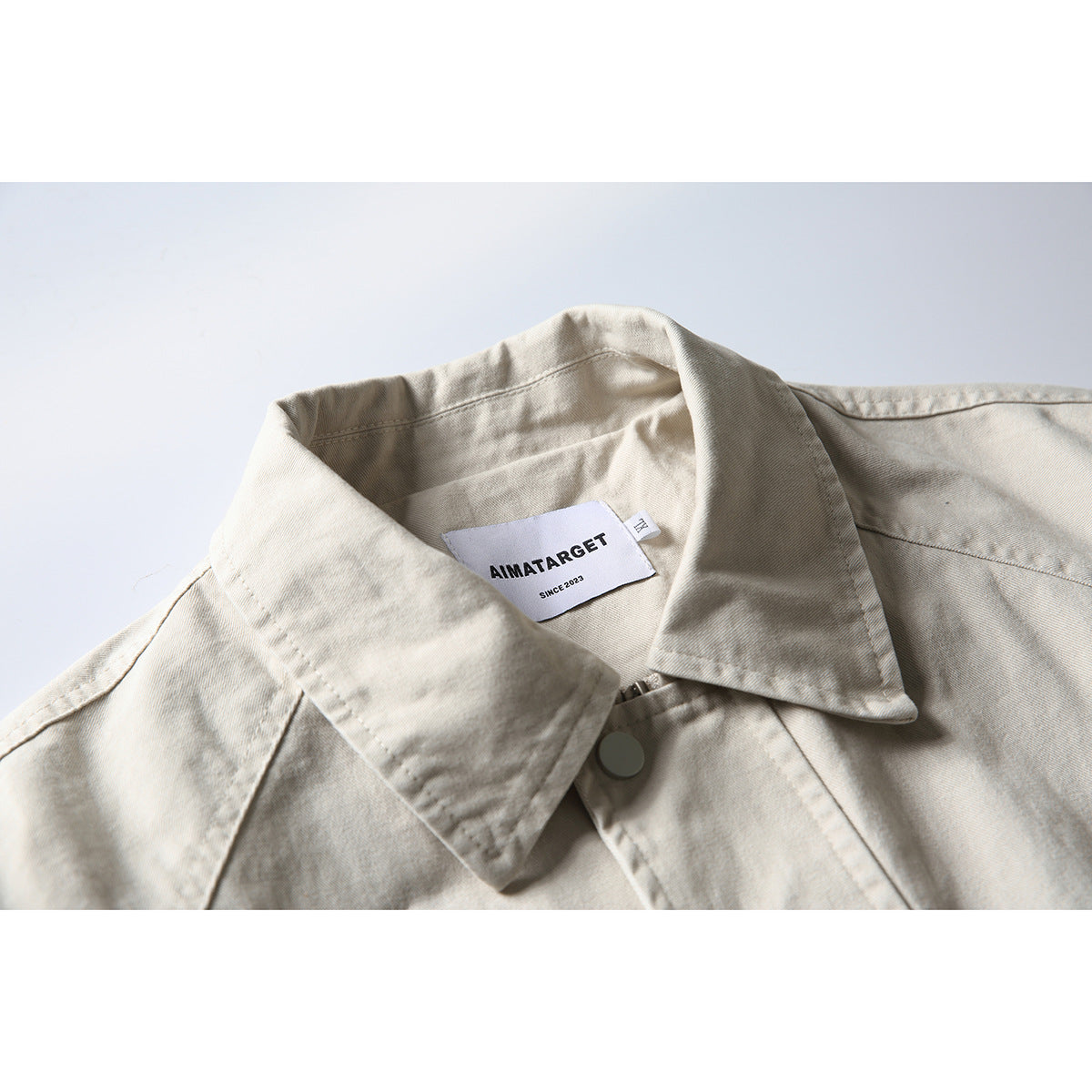 Close-up of an off-white jacket collar, front snap, stitching, and sewn AIMATARGET label.