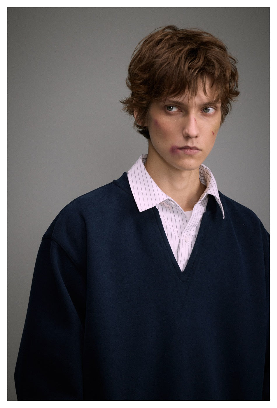 Close-up of a model wearing a navy V-neck sweatshirt layered over a pale pink striped collared shirt.