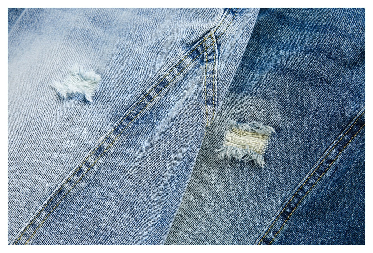 Close-up of frayed distressed patches on light and dark blue denim jeans.
