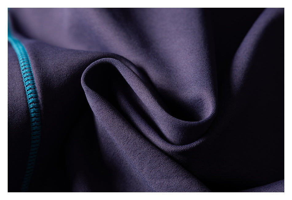 Close-up of dark purple fabric folds with a line of bright teal stitching along the left edge.