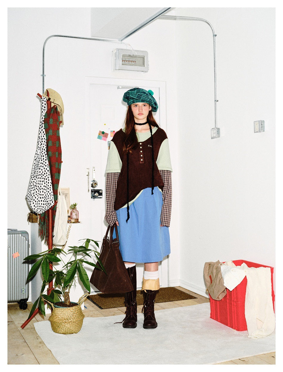 Front view of a model wearing a brown sleeveless top over layered shirts, with a blue skirt and teal plaid beret.