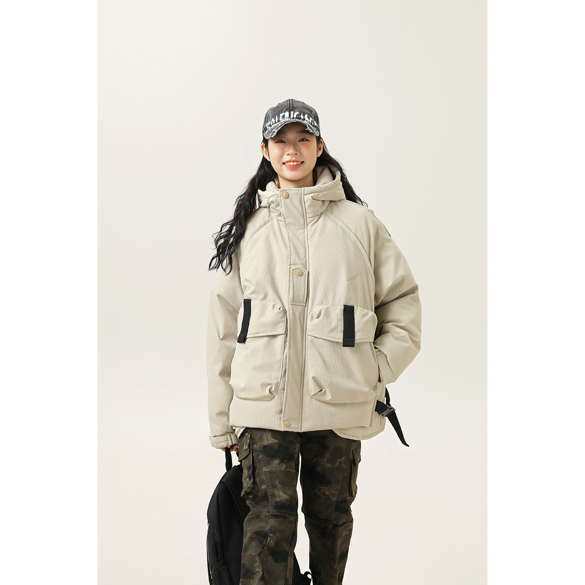 Model wearing a light beige hooded jacket with large flap pockets and black trim, shown from the front.