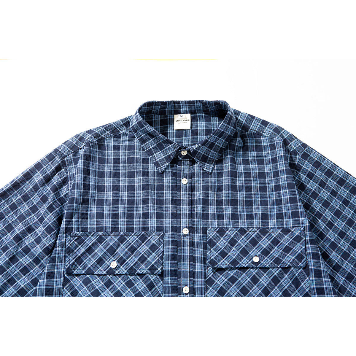 Close-up of a navy plaid short-sleeve button-up shirt with two large diagonal-plaid flap pockets.