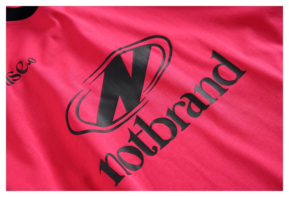 Close-up of a large black printed emblem and lettering on the bright pink T-shirt front.