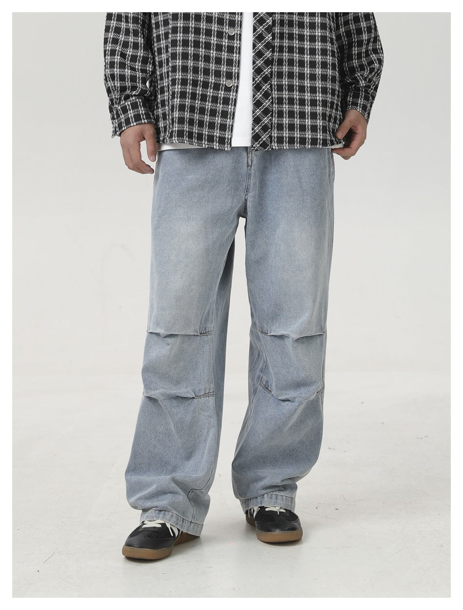 Person wearing light-blue wide-leg pleated-knee jeans with a plaid shirt and black sneakers, angled view