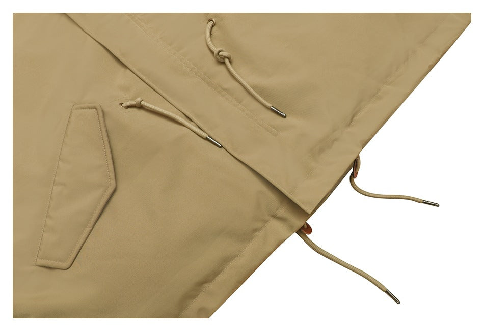Close-up of a tan jacket’s lower front, showing flap pockets and adjustable drawcords with metal tips.