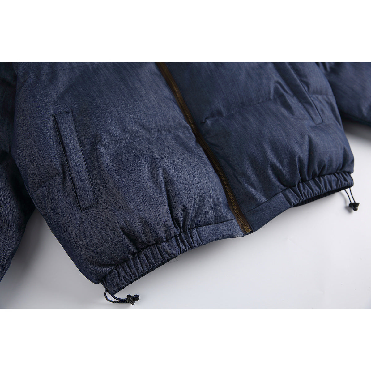 Close-up of a navy padded jacket showing the front zipper, vertical pockets, and gathered hem with drawcords.