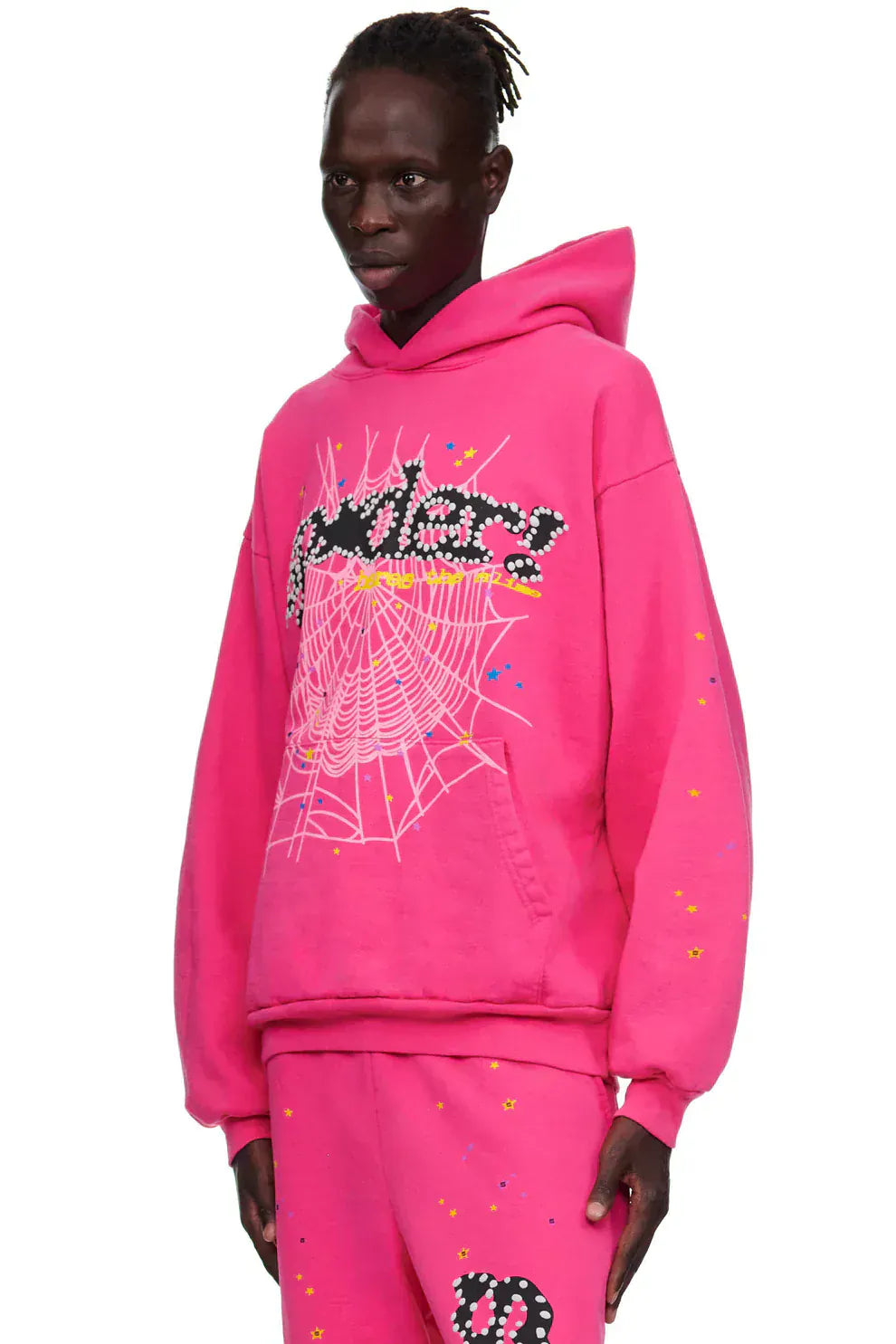A person wears the Sp5der “Nevermind the Punk” Hoodie – Hot Pink 440GSM Heavyweight Streetwear Pullover and matching pants with web and floral graphics, standing against a plain white background.