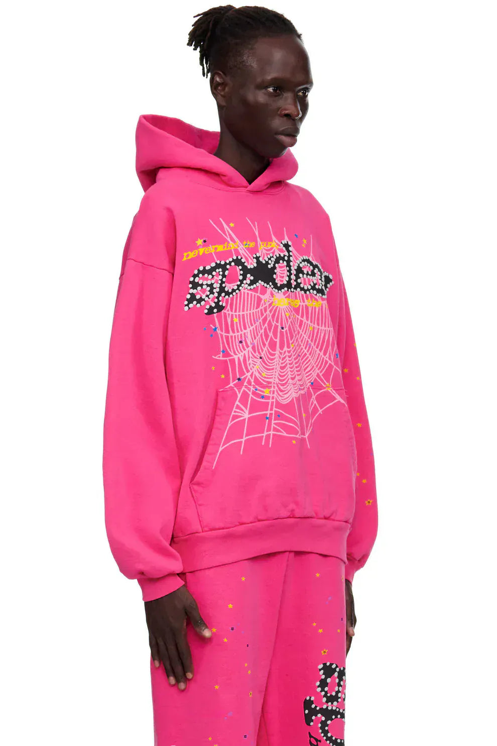 Someone wears the Sp5der “Nevermind the Punk” Hot Pink 440GSM Heavyweight Streetwear Hoodie with matching pants, featuring web and "Spider" graphics for a bold Y2K punk look against a plain background.