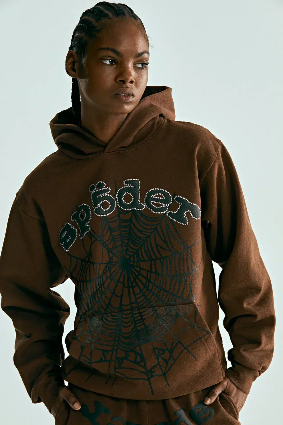 A person wearing a Sp5der Web Hoodie – Mocha Brown 440GSM Heavyweight Streetwear Pullover, featuring a black spiderweb and the word "spēder" in stylized white lettering on the front.