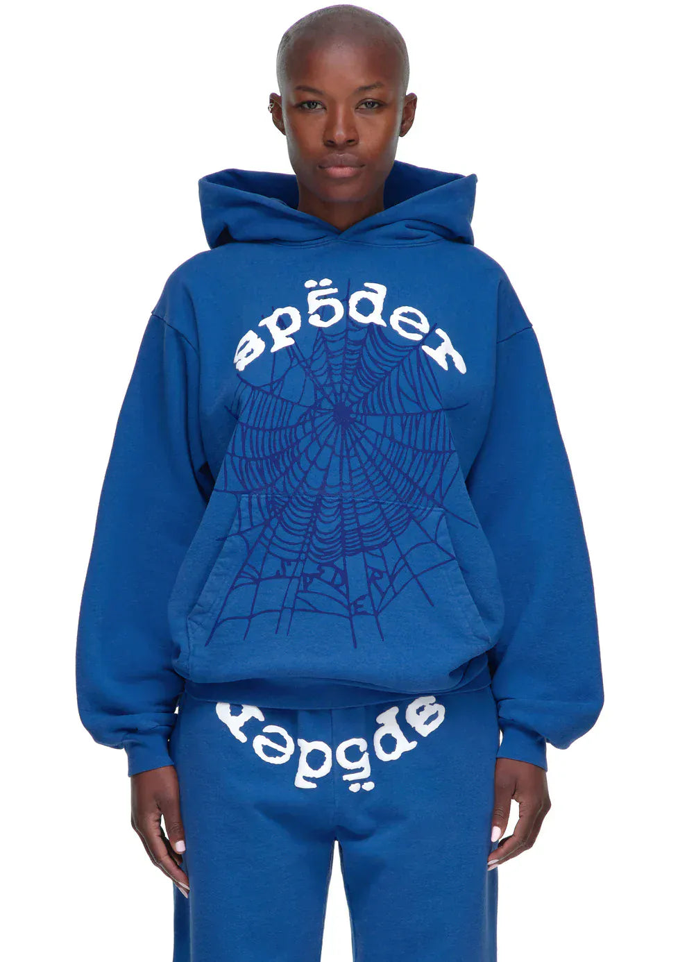 Wearing the Sp5der OG Web Hoodie 440GSM in royal blue, a heavyweight cotton fleece sweatshirt featuring a white spider-web graphic and "spēder" text.
