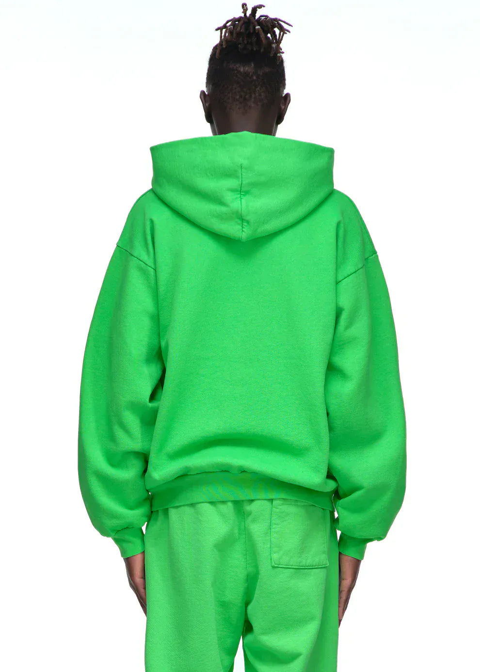 A person stands facing away, wearing a neon green Sp5der “Web Core” Hoodie – a 440GSM heavyweight oversized streetwear pullover – and matching sweatpants for an eye-catching look.