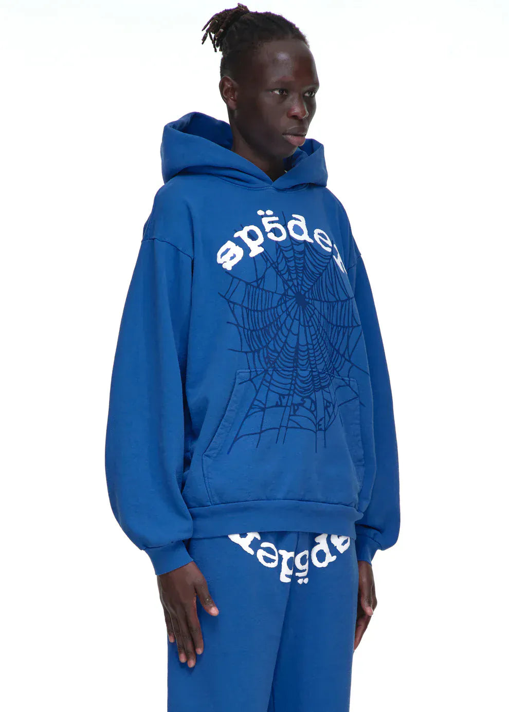 Person wearing the Sp5der OG Web Hoodie 440GSM – Royal Blue Heavyweight Spider-Web Graphic Sweatshirt and matching sweatpants with white stylized text, standing against a plain white background.